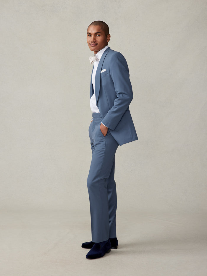 Man in lake blue tuxedo, side profile with hand in pocket, navy velvet loafers