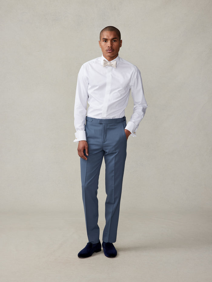 Man in white shirt, ivory bow tie, and lake blue tuxedo trousers, full-length front view