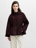 A woman wearing a brown faux suede cinched waist coat with raglan sleeves, side pockets and a button down fastening.