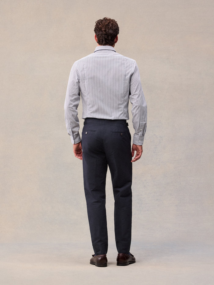 A man in deepwater navy linen trousers and a striped shirt, back view, full length.