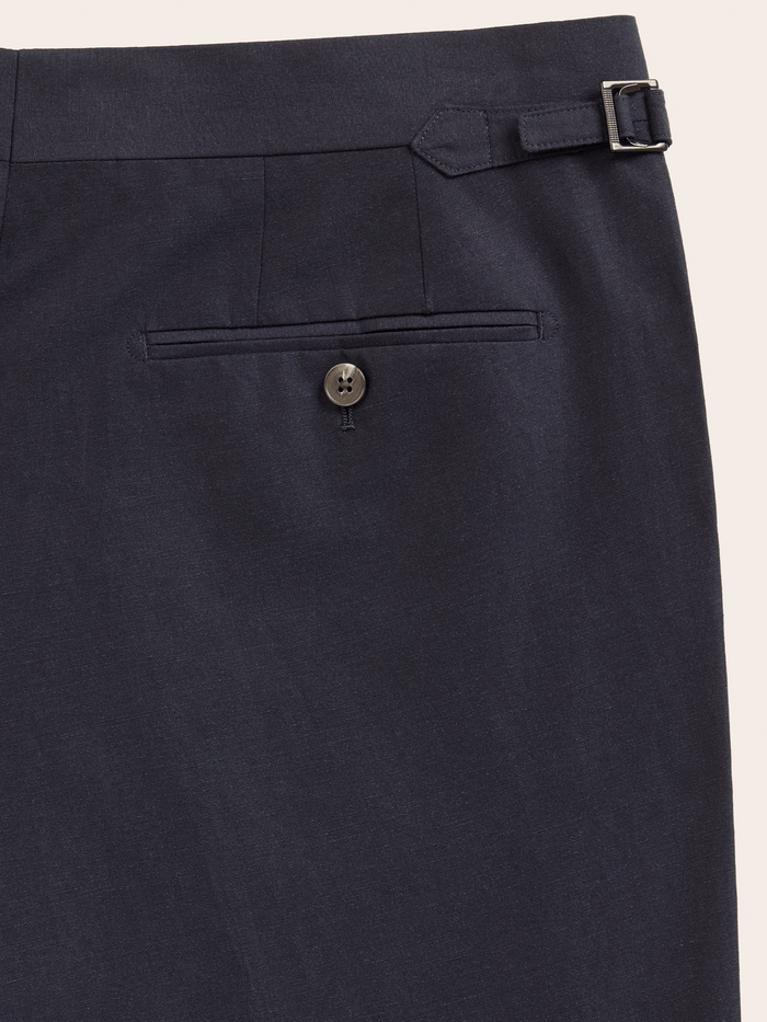 Close-up of a deepwater navy linen trousers buttoned welt back pocket and side-adjuster.