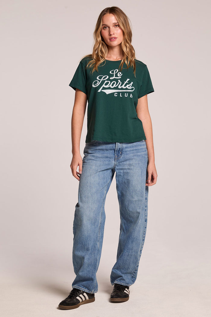 Front view of a woman wearing the Chaser Le Sports Club Tee and sneakers on a neutral background