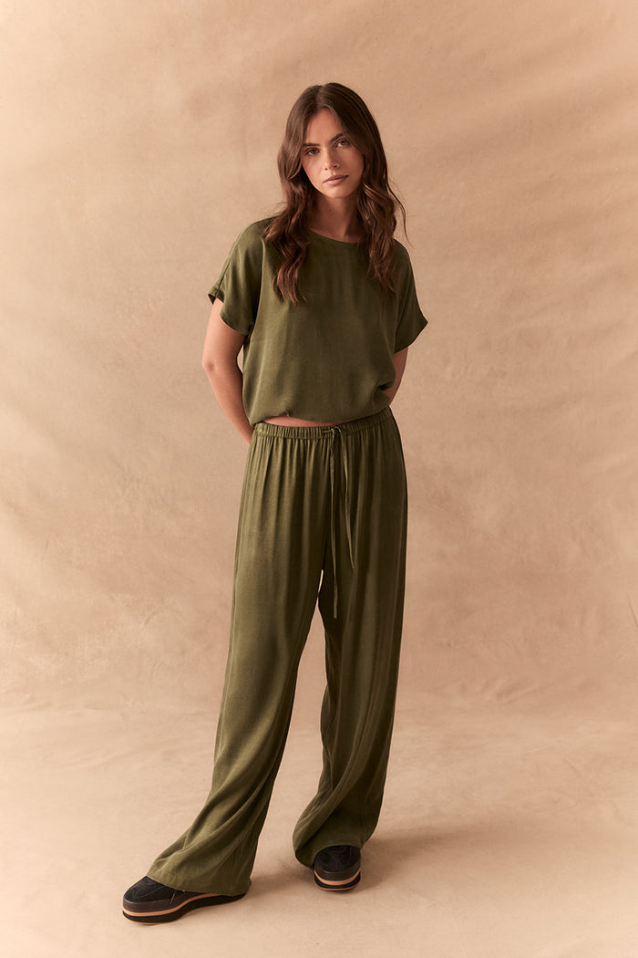 Full front view of Lee Trouser in bronze green with wide-leg silhouette and relaxed drape with matching tee against a beige background