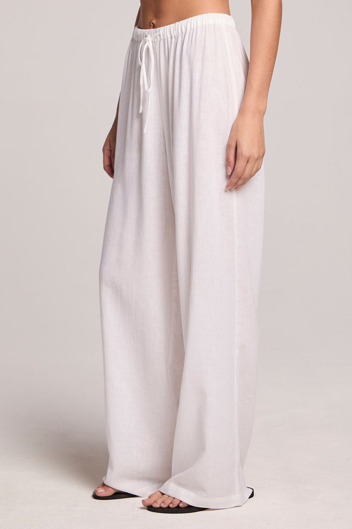 A side angle view of a woman wearing the Chaser Lee White Trouser  and black shoes on a neutral background