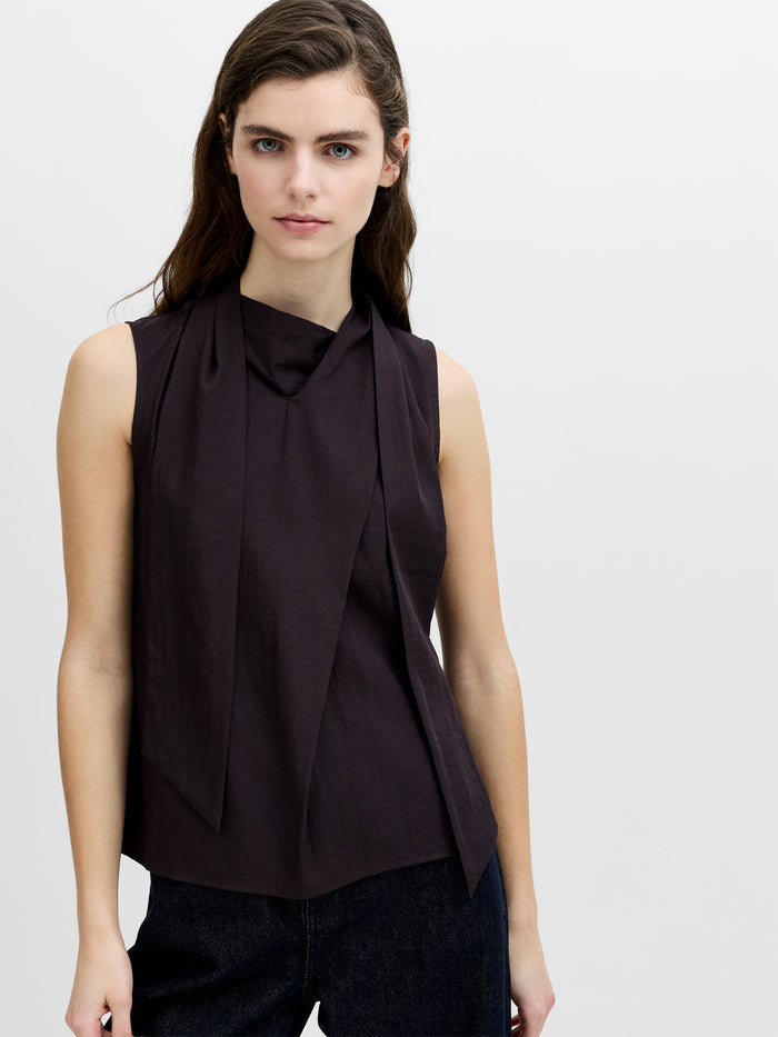 A woman wearing a brown sleeveless top with a draped scarf at the neckline.