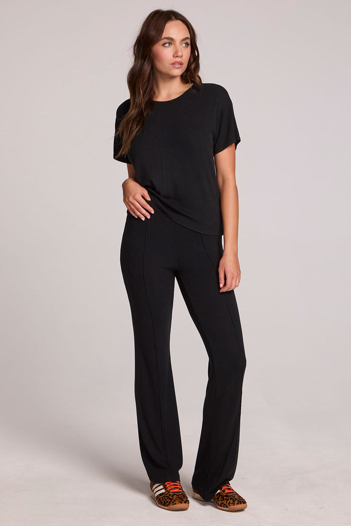 Full body view of a woman wearing the Chaser Leonor Black Tee on a neutral background with black pants and hands down at sides