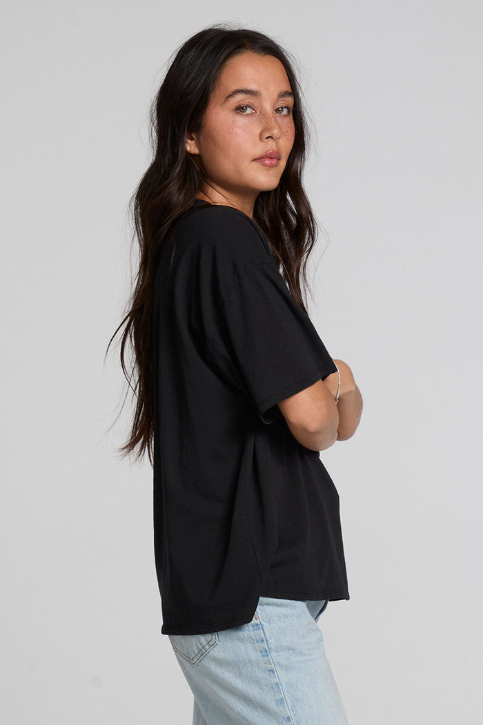 Side view of a woman wearing the Chaser Let's Get Spooky Tee on a neutral background with blue jeans