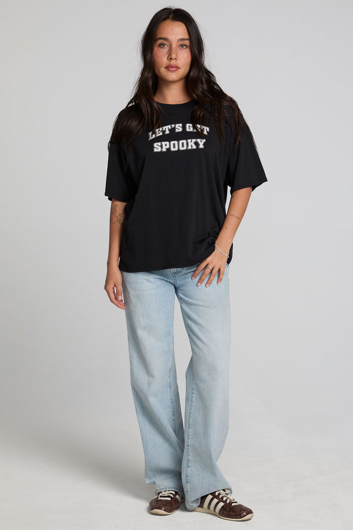 A full body front view of a woman wearing the Chaser Let's Get Spooky Tee on a neutral background