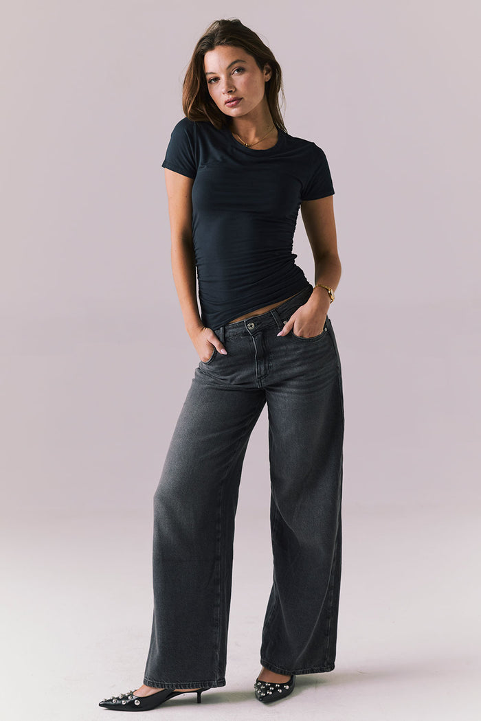Full body view of Chaser Brand Louiss Licorice Black Tee styled with wide leg charcoal jeans and black pointed heels