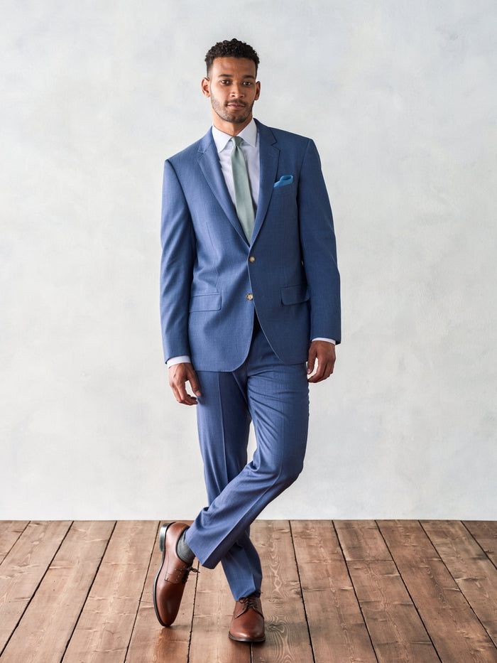 Man in light blue suit, sage tie, and brown shoes, walking pose