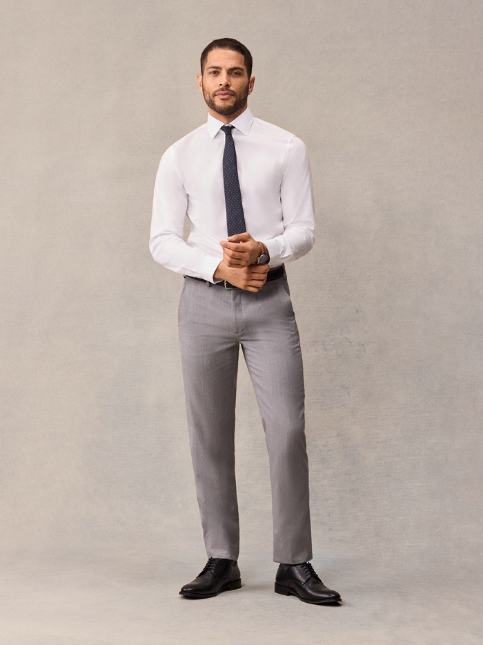 Man in white dress shirt, navy pindot tie, and light grey trousers, front view