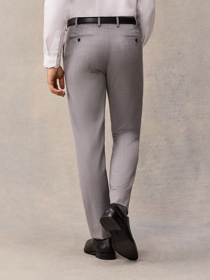 Back view of man in light grey suit trousers with black belt, walking pose