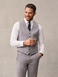 Smiling man in light grey suit vest, black pindot tie, hand raised