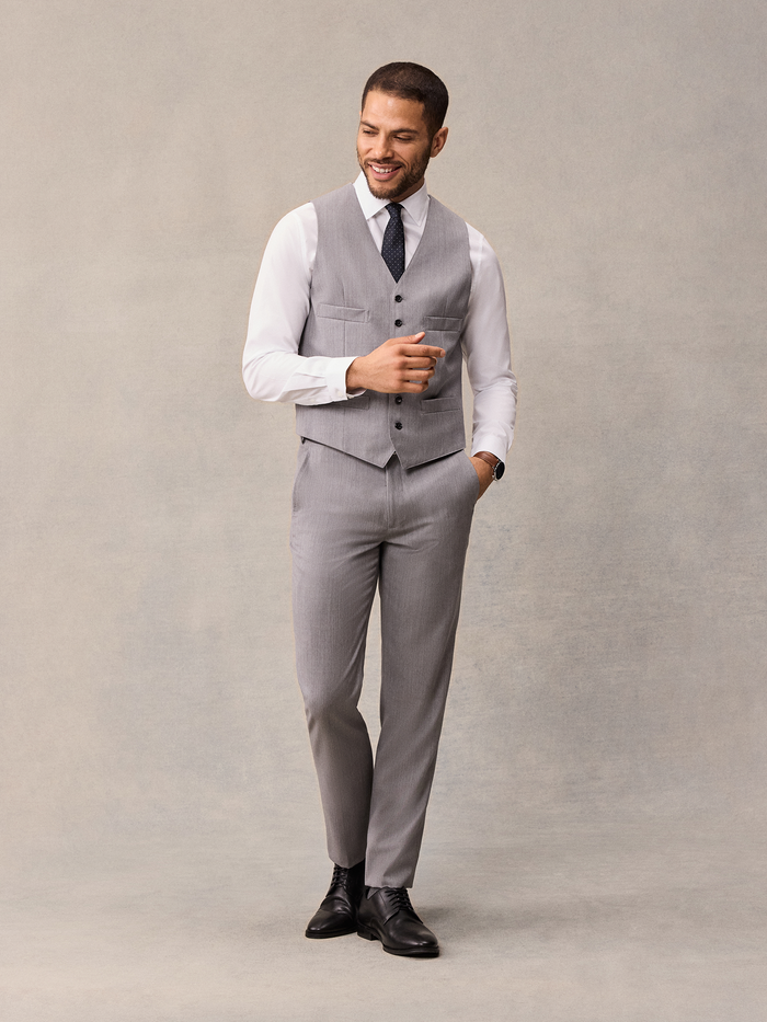 Smiling man in light grey suit vest, black pindot tie, walking pose