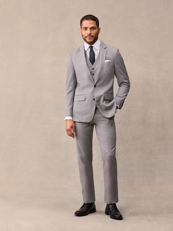 Man in light grey three-piece suit, navy pindot tie, hand in pocket