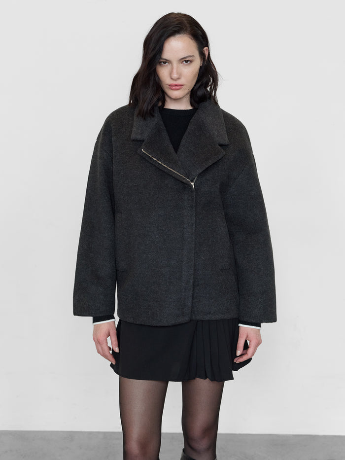 A woman wearing a dark grey coat with drop shoulders, long sleeves, an over sized lapel collar and a bomber fit.