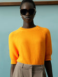 Woman wearing a bright orange, short sleeve textured knitted jumper with a crew neck, ribbed cuffs and a ribbed hem