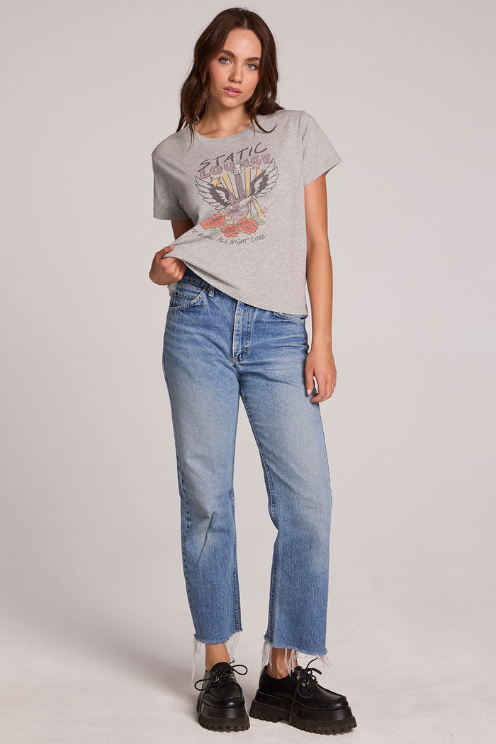 Full body front view of a woman wearing the Chaser  Live Music Graphic Tee and blue jeans on a neutral background with hand on hip