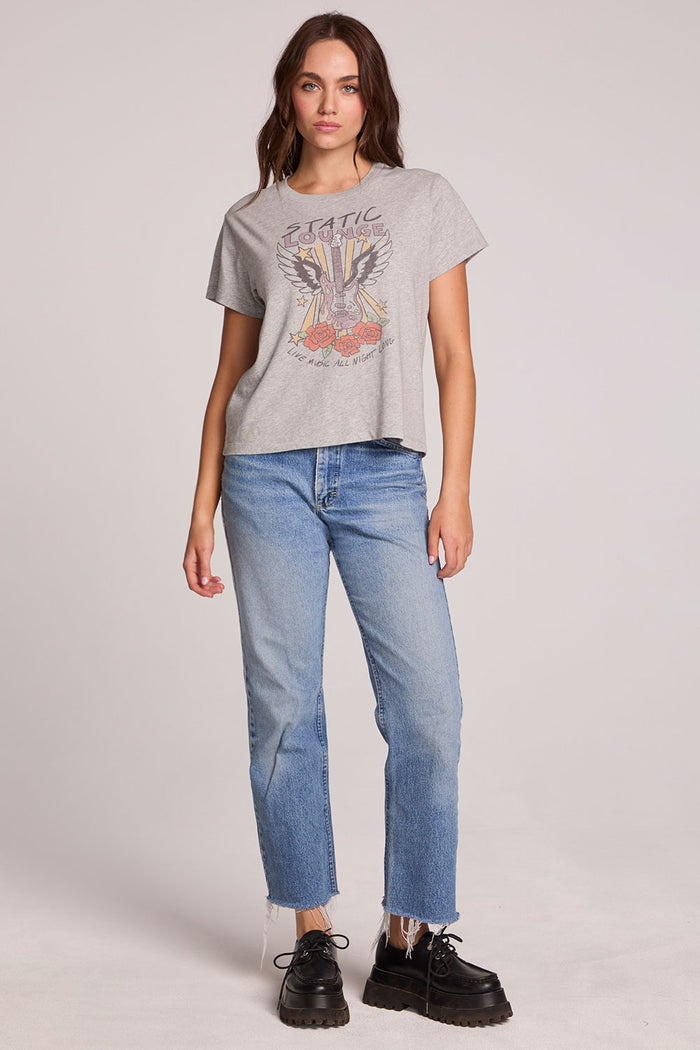 Full body front view of a woman wearing the Chaser  Live Music Graphic Tee and blue jeans on a neutral background with hands lowered