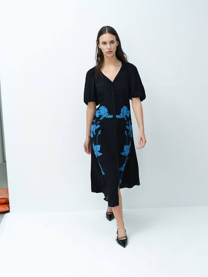 A woman wearing a blue floral midi dress with a V-neck, short sleeves and a button through fastening.