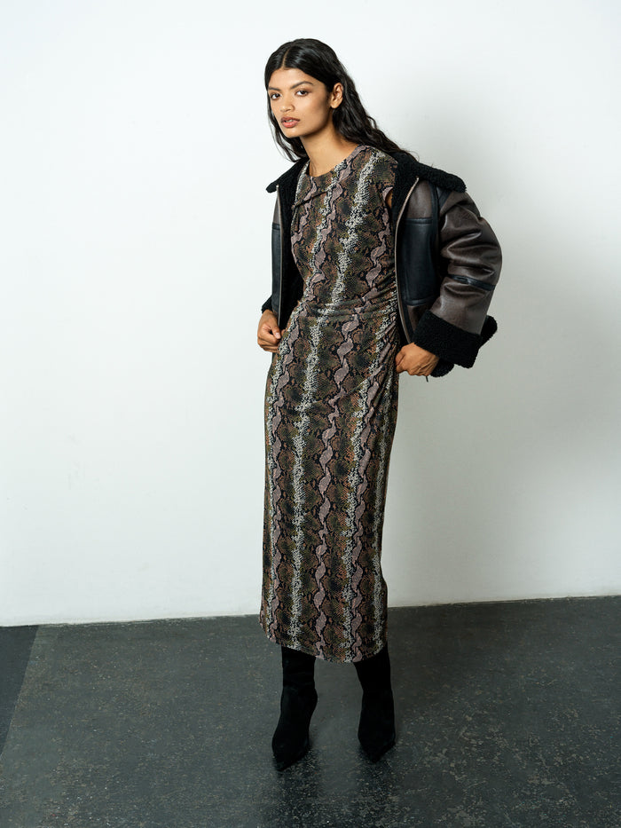 A woman wearing a snakeskin mesh midi length dress with a ruched waist, cap sleeves and a boat neckline.