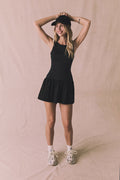 Editorial full body view of Chaser Brand Lou Licorice Black Mini Dress styled with cap and sneakers