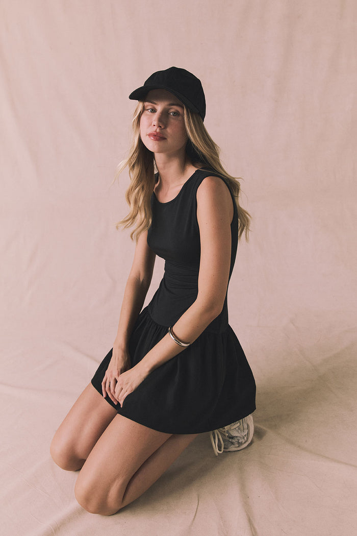 Editorial seated view of Chaser Brand Lou Licorice Black Mini Dress showing soft stretch fabric and fitted waist