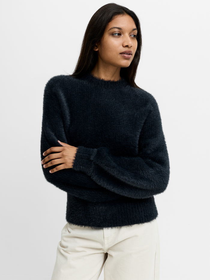 A woman wearing a dark grey fluffy jumper with a crew neck, long sleeves and a relaxed fit.