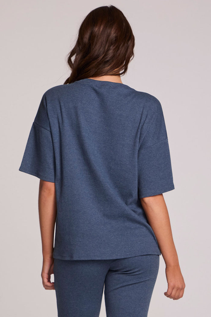 Back view of a woman wearing the Chaser Lunnah Dark Denim Top and blue pants on a neutral background