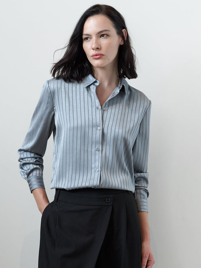 A woman wearing a grey shirt with a shirt collar, long sleeves and a stripe pattern.