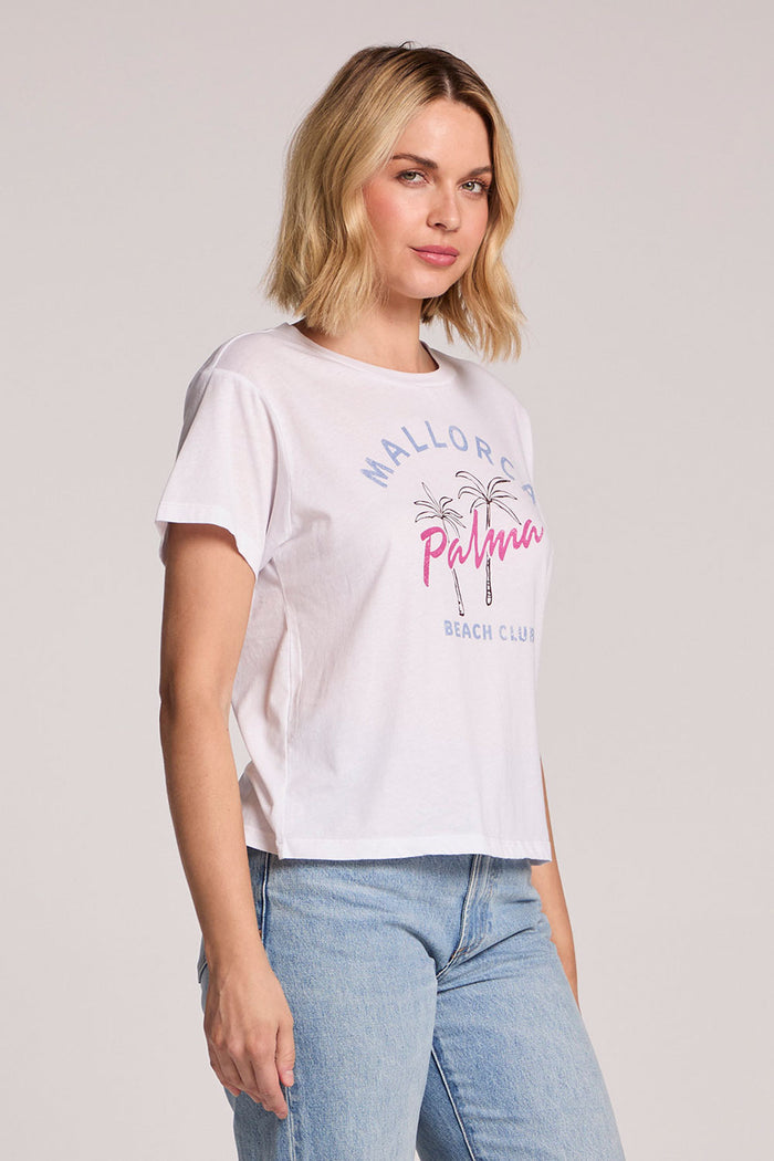 Side angle view of a woman wearing the Chaser  Mallorca Beach Club Tee on a neutral background with arms at her sides