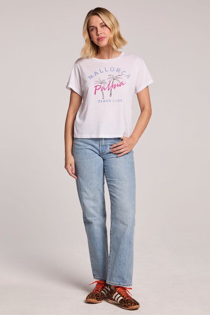 Front view of a woman wearing the Chaser  Mallorca Beach Club Tee and sneakers on a neutral background