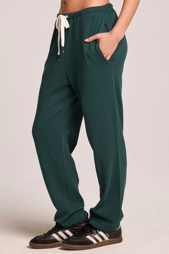 Side view of a woman wearing the Chaser   Manhattan Pine Joggers on a neutral background with hands in her pockets