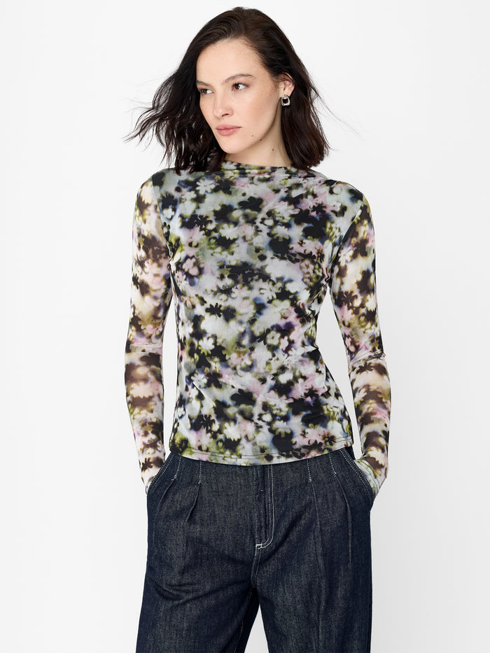 A woman wearing a floral print mesh top with long sleeves, ruched shoulders and a high crew neck.