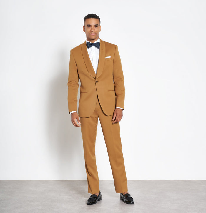 Man in marigold shawl-lapel tuxedo jacket, navy bow tie, and black loafers, white background