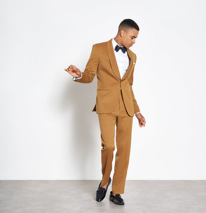 Man in marigold shawl-lapel tuxedo suit, navy bow tie, looking down mid-stride