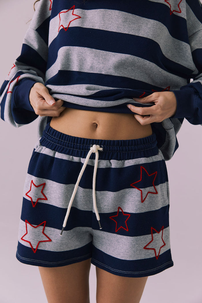 Front mid-detail of Chaser Brand Maritime Stars Shorts in Heather Grey Stripe with model lifting pullover to show waistband fit