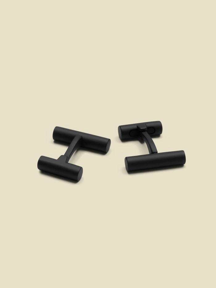 Two black cufflinks on a light beige background.