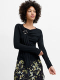 A woman wearing a black top with long sleeves, a draped neckline, a metal ring detailing and a fitted silhouette.