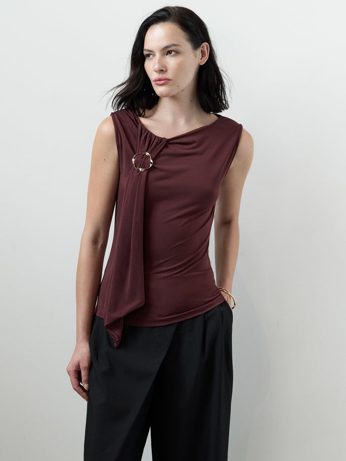A woman wearing a soft burgundy sleeveless Top with a draped neckline, a metal ring detail and a fitted silhouette.