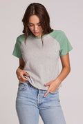 Front view of a woman wearing the Chaser Maybel Verdelle and Heather Grey Raglan Tee and bluejeans on a neutral background with hand in pocket