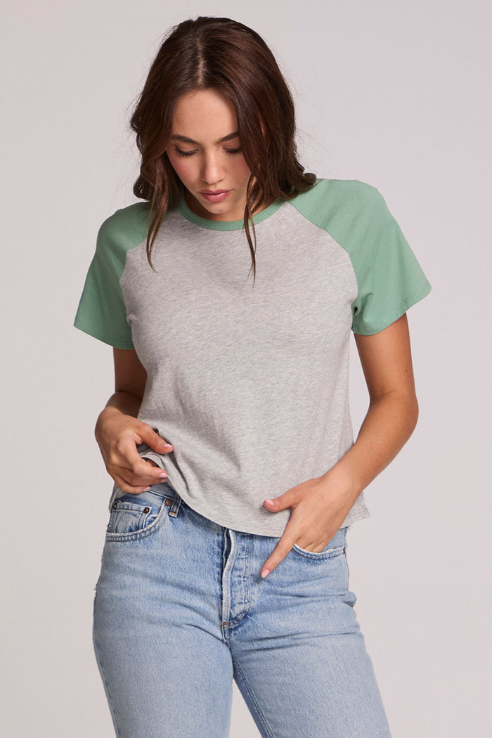 Front view of a woman wearing the Chaser Maybel Verdelle and Heather Grey Raglan Tee and bluejeans on a neutral background with hand in pocket