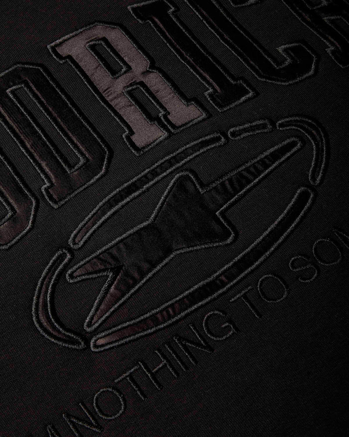 Close-up of a black fabric surface with large tonal embroidered lettering and a star-like emblem, showing partial text.