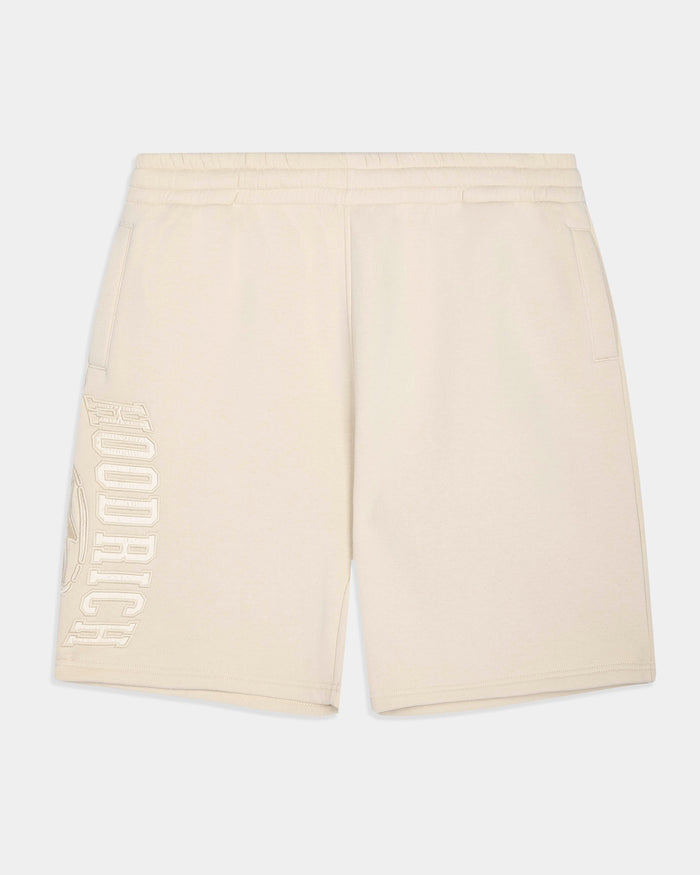 Cream-colored athletic shorts with a vertical 'HOODRICH' logo printed in tonal cream on the left leg, shown against a light gray background.