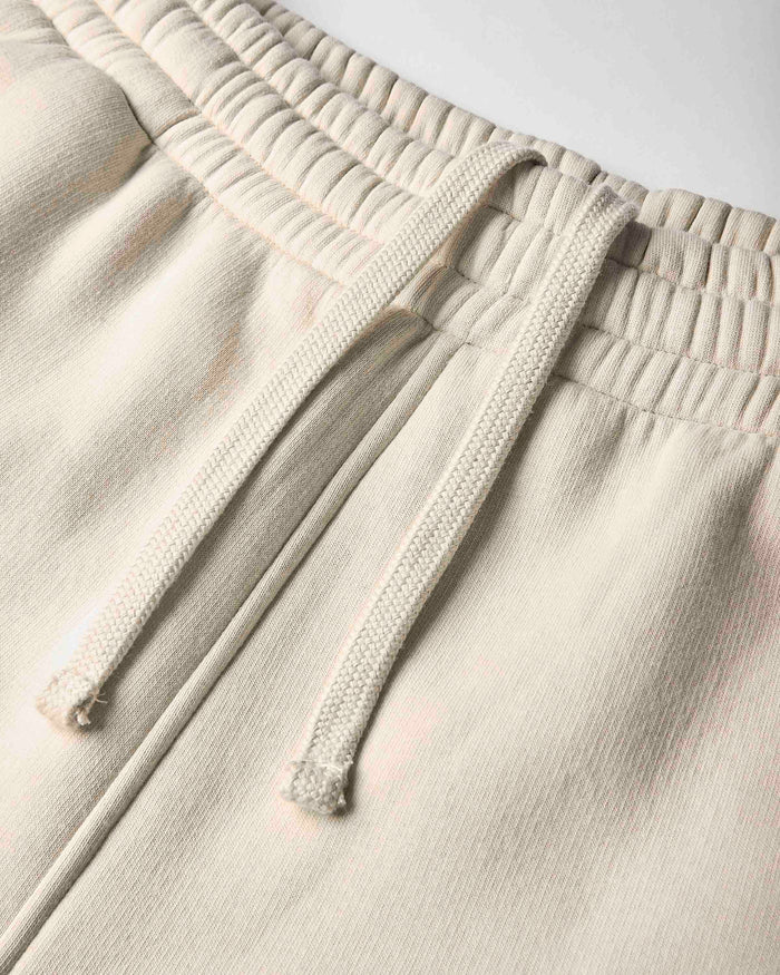 Close-up of a pair of light beige or cream sweatpants showing the textured fabric, elastic waistband, and matching drawstrings.