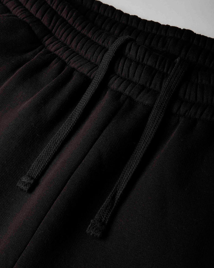Close-up of black drawstring sweatpants showing the elastic waistband and textured drawstrings.