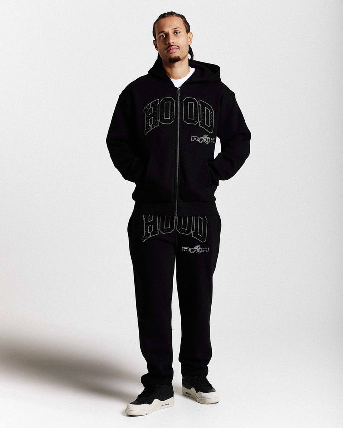 Person wearing a black 'HOODRICH' branded tracksuit on a white background