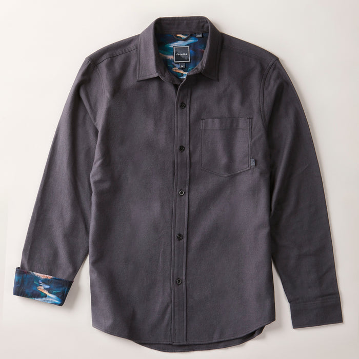 The Men's Cascade Flannel Shirt in Charcoal Grey is a modern-cut, long-sleeve button-up made from Portuguese cotton flannel. It features a chest pocket, collar, and blue-brown abstract pattern inside the cuffs and collar. Laid flat on a light surface.