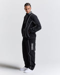Person wearing a black tracksuit with white piping on a light gray background