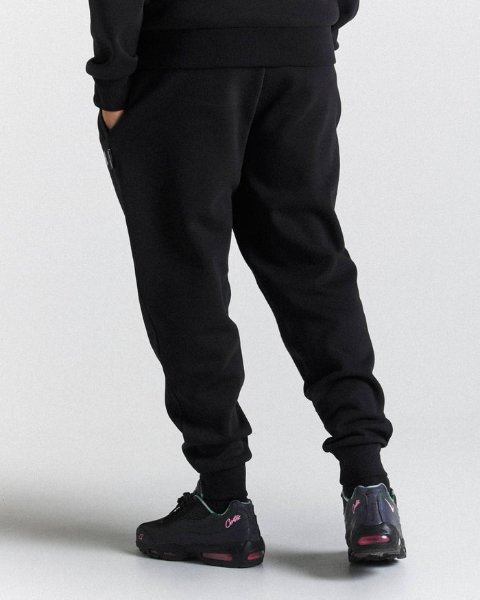 Black jogger sweatpants worn by a model, shown from the back and side against a light gray studio background. The model is also wearing black sneakers.